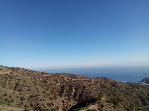 Photograph of Catalina Island. The foreground includes view of the mountains and background of the ocean with clear blue skies